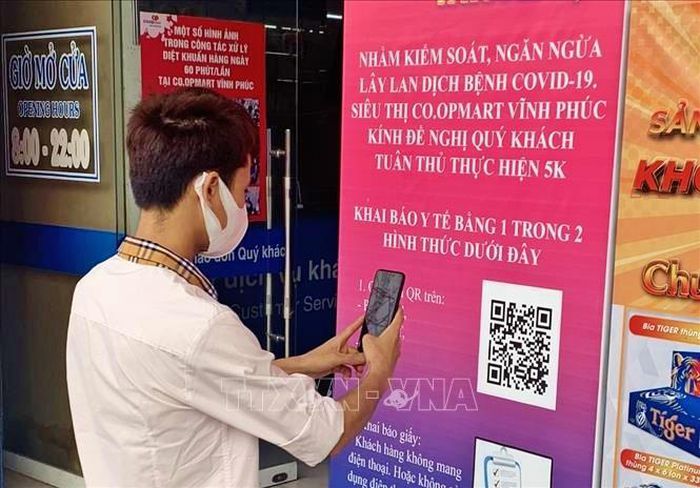 Khách hàng thực hiện quét mã QR khai báo y tế trước khi vào siêu thị Co.opmart Vĩnh Phúc. Ảnh: TTXVN